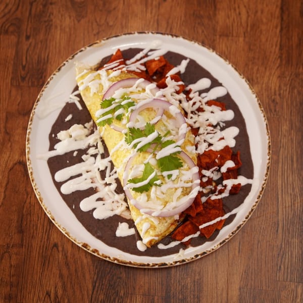 Mexican-style folded tortilla topped with cabbage, red onion, cilantro, and crema, served over black beans with crispy red tortilla chips.
