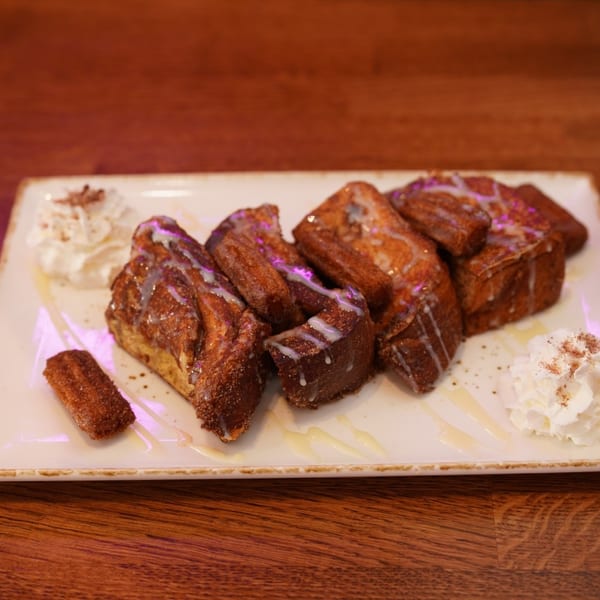 French toast slices drizzled with icing, served with whipped cream and cinnamon on a rectangular plate.