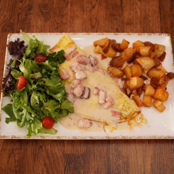 Seafood omelet with creamy sauce, roasted potatoes, and mixed green salad on a rectangular plate atop a wooden table.