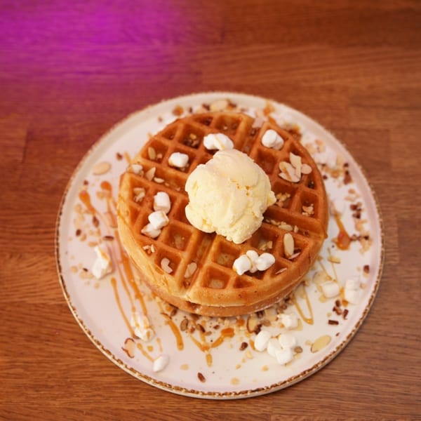 Golden waffle topped with vanilla ice cream, chopped nuts, marshmallows, and caramel drizzle on a plate.