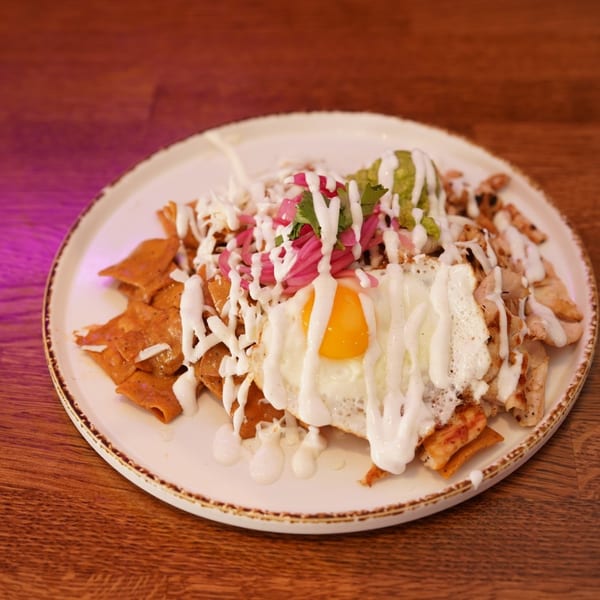 Loaded plate of crispy chips topped with a fried egg, grilled chicken, pickled onions, guacamole, herbs, and creamy sauce.