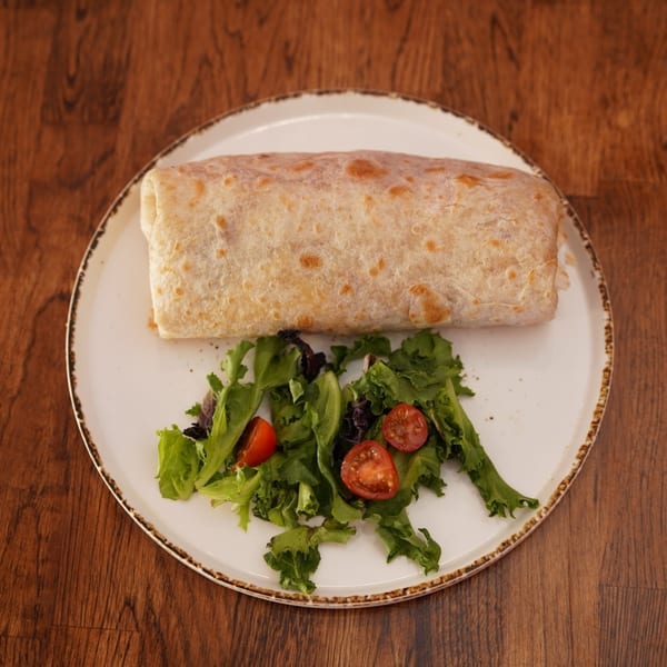 Grilled burrito served with a fresh leafy green salad and halved cherry tomatoes on a white plate.