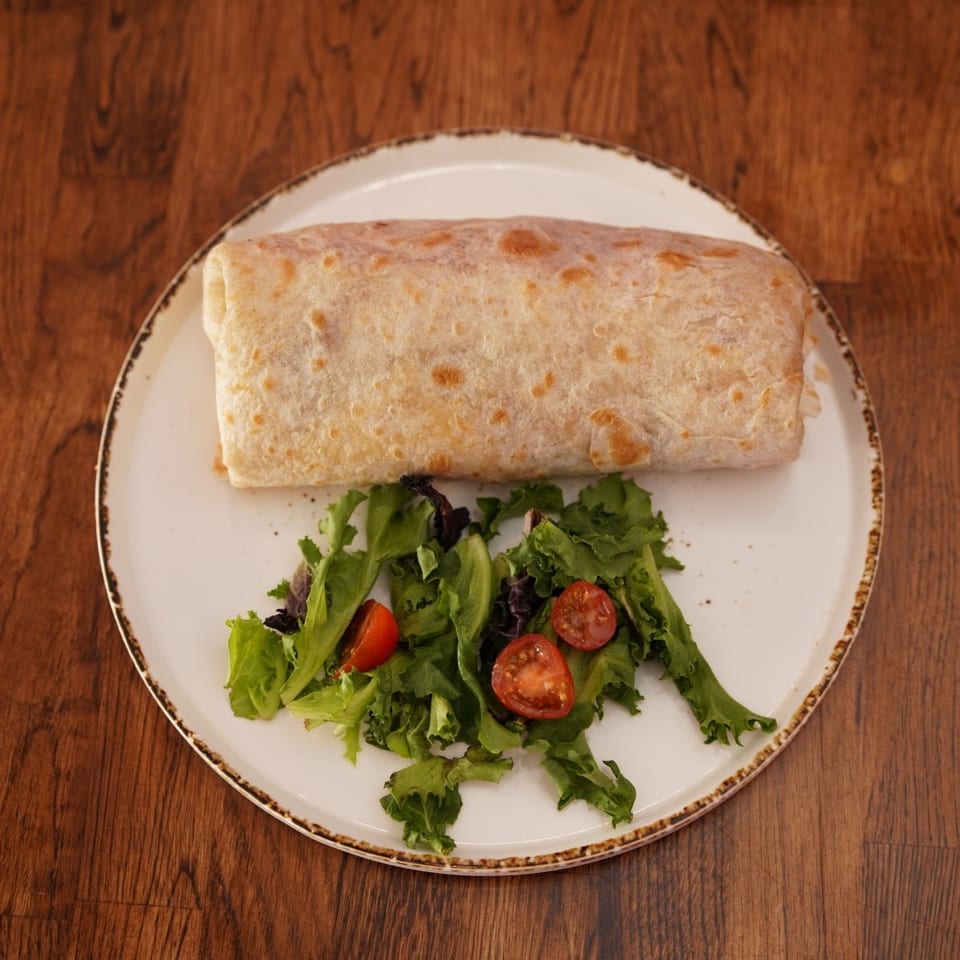 Grilled burrito served with a fresh leafy green salad and halved cherry tomatoes on a white plate.